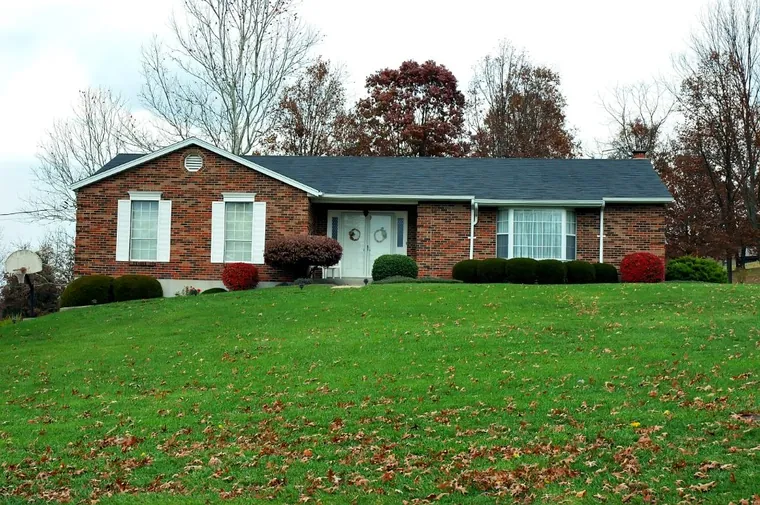 A single-story brick ranch home on a sloping autumn lawn