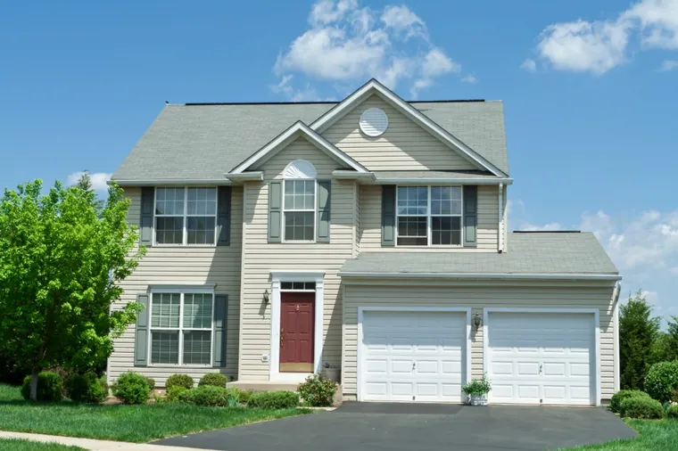 A tan-sided two-story home with a two-car garage and red front door